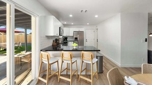 A modern kitchen with a central island, bar stools, and a dining area with a table and chairs. - Sleeps 16 | Heated Pool + Arcade + Backyard Resort (Mesa)
