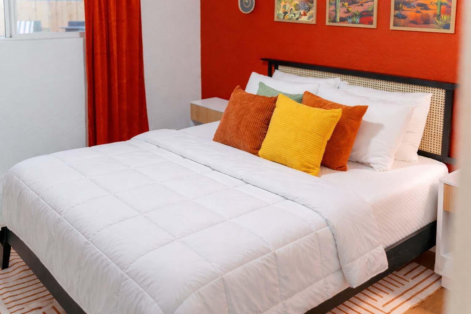 Un lit avec une couette blanche, des oreillers orange et jaunes, et une tête de lit en bois.
