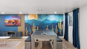 A room with a ping pong table, a TV, and a mural of a desert landscape. - Sleeps 16 | Heated Pool + Arcade + Backyard Resort (Mesa)
