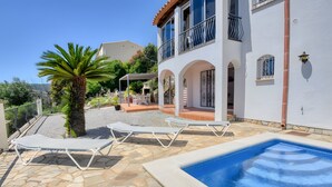 Zona de piscina con sillas de descanso, una palmera y un edificio blanco con balcones.