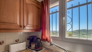 Una cocina con armarios de madera, un tostador, una cafetera y vista a un paisaje verde a través de una ventana con barrotes.
