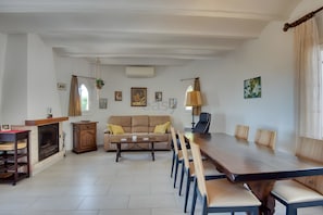 A spacious living area with a large wooden dining table, a beige sofa, and a fireplace.