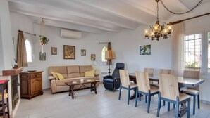 Una sala de estar con sofá, mesa de centro, mesa de comedor con sillas, una araña y obras de arte en la pared.