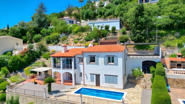 Una villa en la ladera con piscina, varios balcones y abundante vegetación.