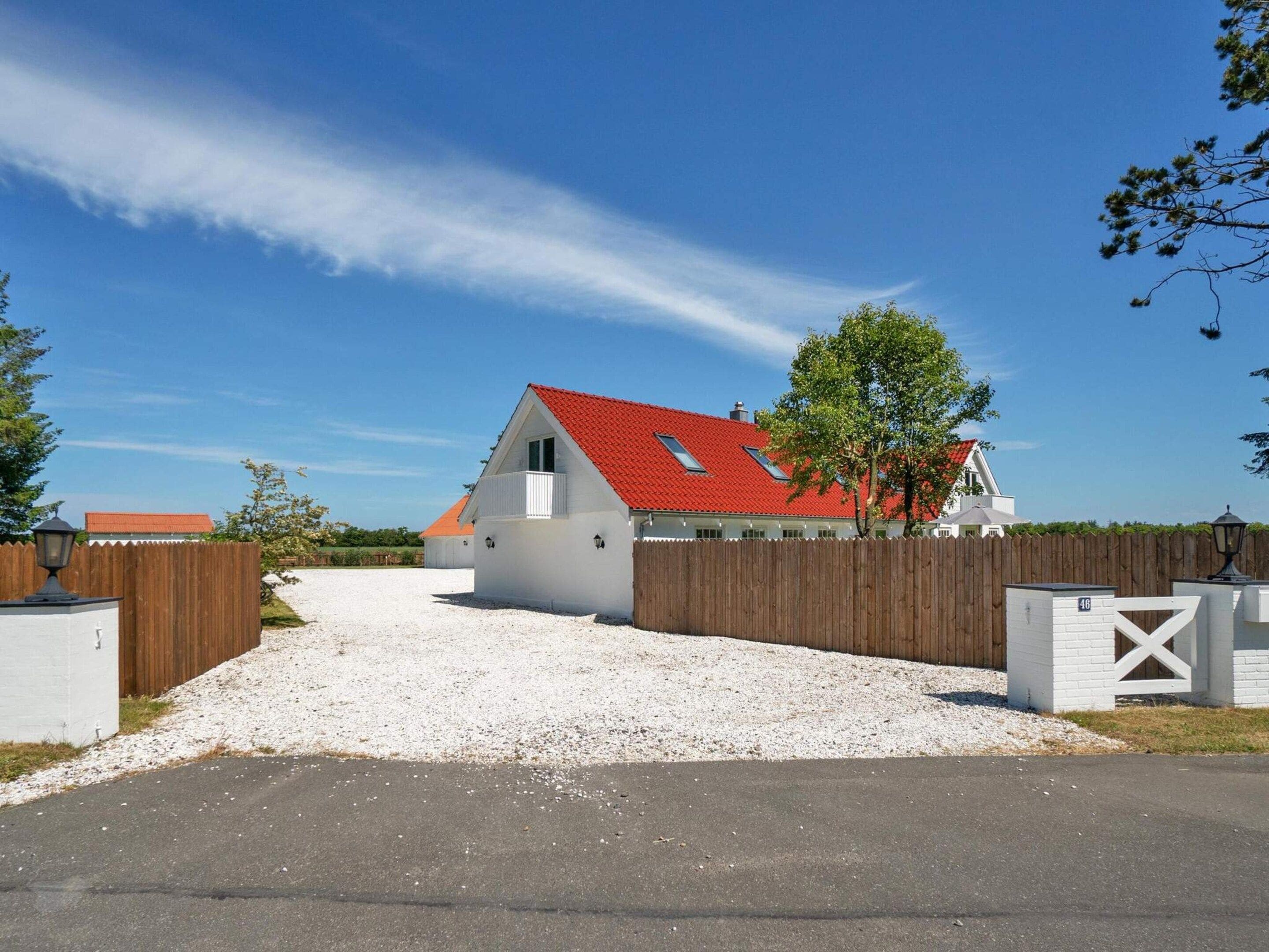 Une maison de plain-pied avec un toit rouge, une allée en gravier et une clôture en bois.