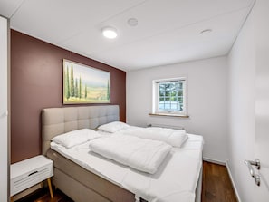 A bedroom with a large bed, a bedside table, a window, and a painting on the wall. - 4 Star Holiday Home in Lokken (Lokken)