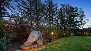 Una escultura en un jardín con una valla de madera y árboles al fondo.