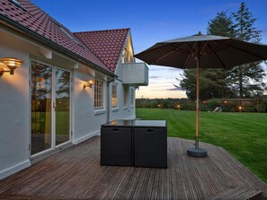 A wooden deck with a patio table and umbrella, a house with a red roof, and a well-lit exterior. - 4 Star Holiday Home in Lokken (Lokken)
