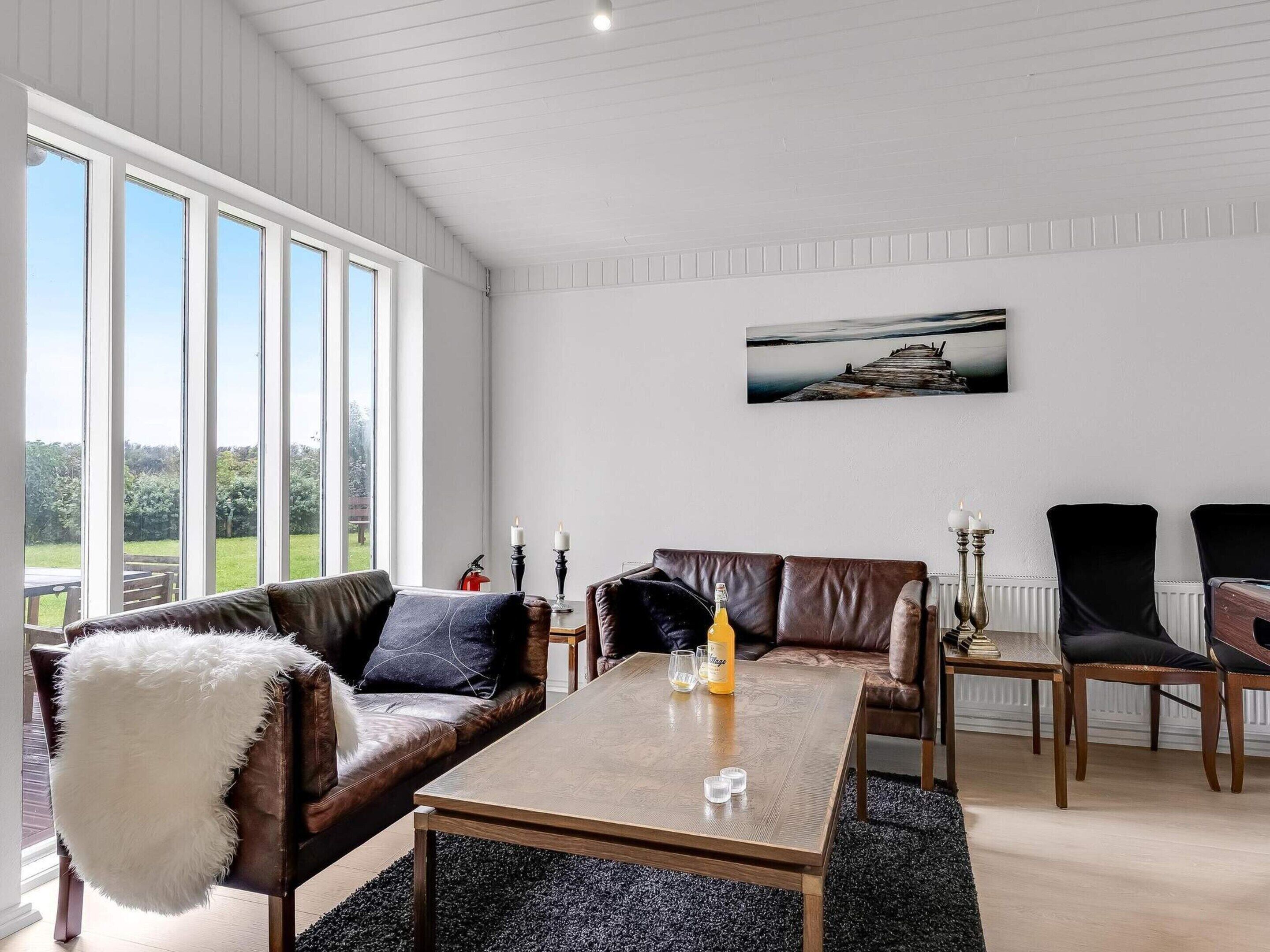 Een ruime kamer met een groot raam, een houten salontafel, leren banken en uitzicht op het landschap.