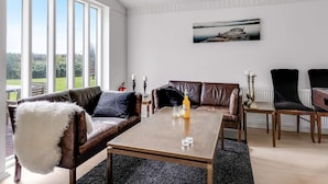 Una habitación amplia con un gran ventanal, una mesa de centro de madera, sofás de cuero y vistas al exterior.