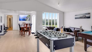 Una habitación amplia con una mesa de fútbolín, un comedor con sillas y una mesa, y un ventanal que ofrece vistas al exterior.