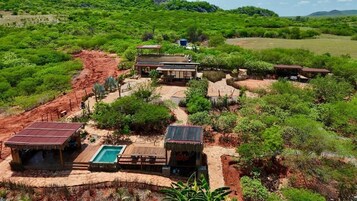 A remote eco-lodge with a pool, thatched-roof structures, and a natural landscape.