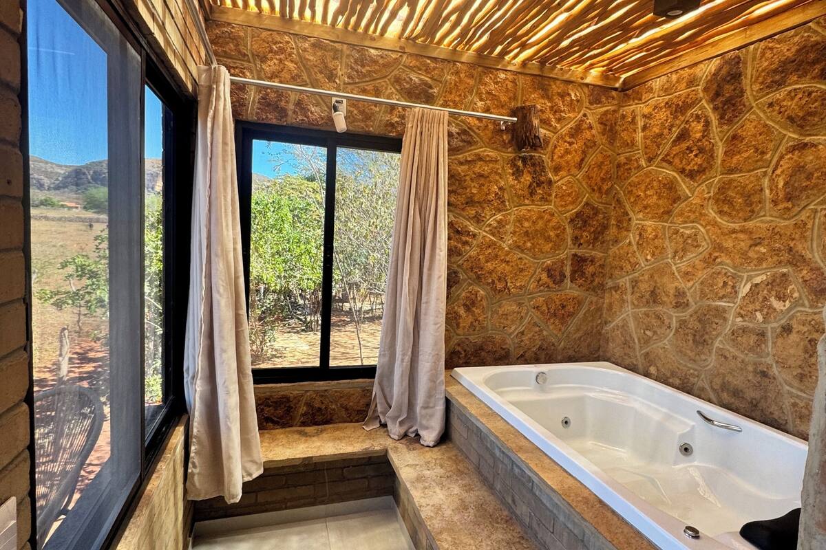 Ein Badezimmer mit Steinwand, einer Badewanne und einem Fenster mit Vorhängen.