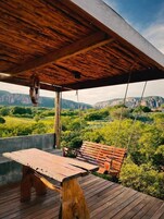 A wooden deck with a swing chair, a picnic table, and a hanging light fixture.