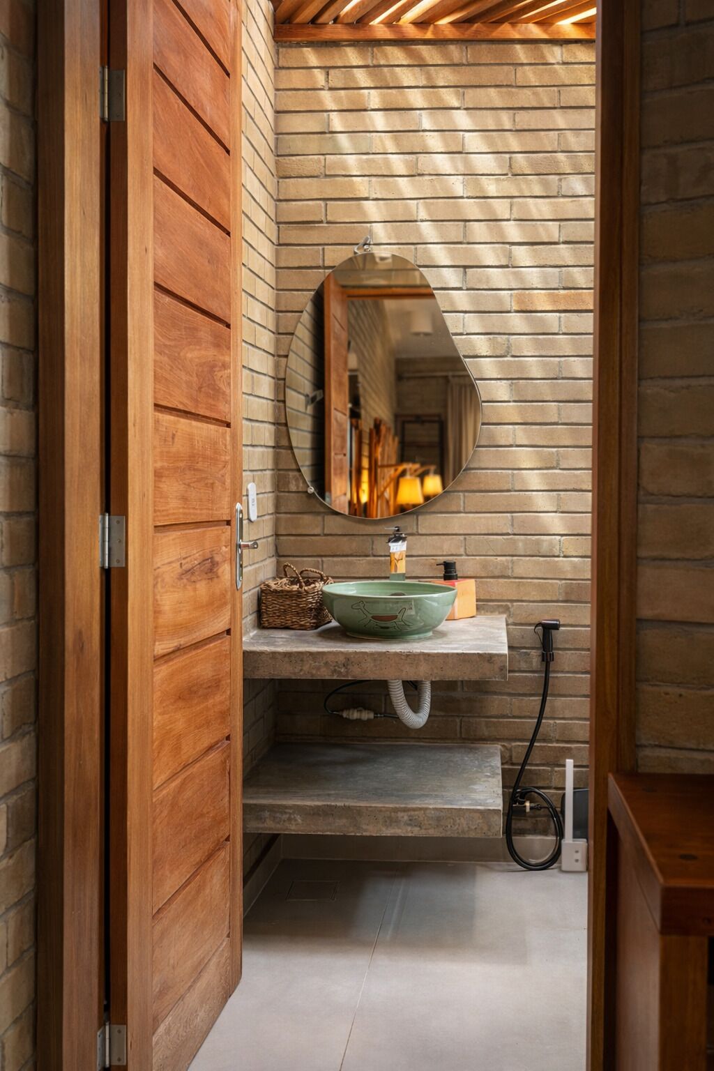 A bathroom with a wooden door, a green sink, a mirror, and a brick wall.