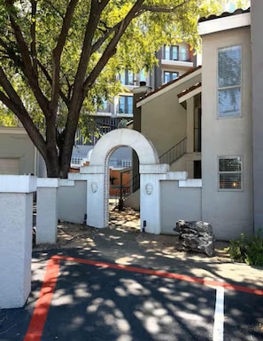 A gated entrance with a stone archway, a paved driveway, and a tree providing shade.