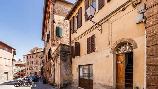 A narrow street with buildings, a wooden door, and a motorcycle parked on the side. - Apartment in the historic center, Close to Piazza del Campo and the Duomo (Siena)