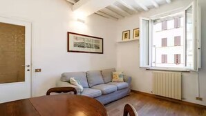 A room with a wooden dining table, a light blue sofa, a radiator, and a window with shutters. - Apartment in the historic center, Close to Piazza del Campo and the Duomo (Siena)