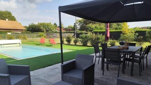 Ein überdachter Außenbereich mit Korbmöbeln, einem Pool und einer Rasenfläche.