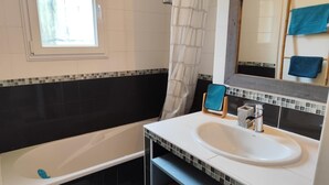 Ein Badezimmer mit einer Badewanne, einem Waschbecken, einem Spiegel und einem Fenster.