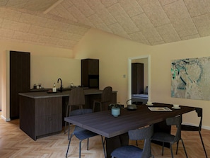 Una cocina moderna con armarios oscuros, piso de madera en patrón de espiga y un comedor con una mesa grande y sillas.
