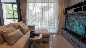 Ein modernes Wohnzimmer mit einer Couch, einem Hocker, einem Beistelltisch und einem Flachbildfernseher.