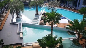 Ein Hotelpool mit mehreren Bereichen, Palmen und Liegestühlen.