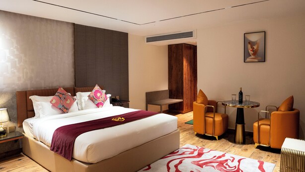 A modern hotel room with a large bed, a small table with chairs, and a wall-mounted air conditioner. - Hotel Golden Amulya Rest Wings (Bengaluru)