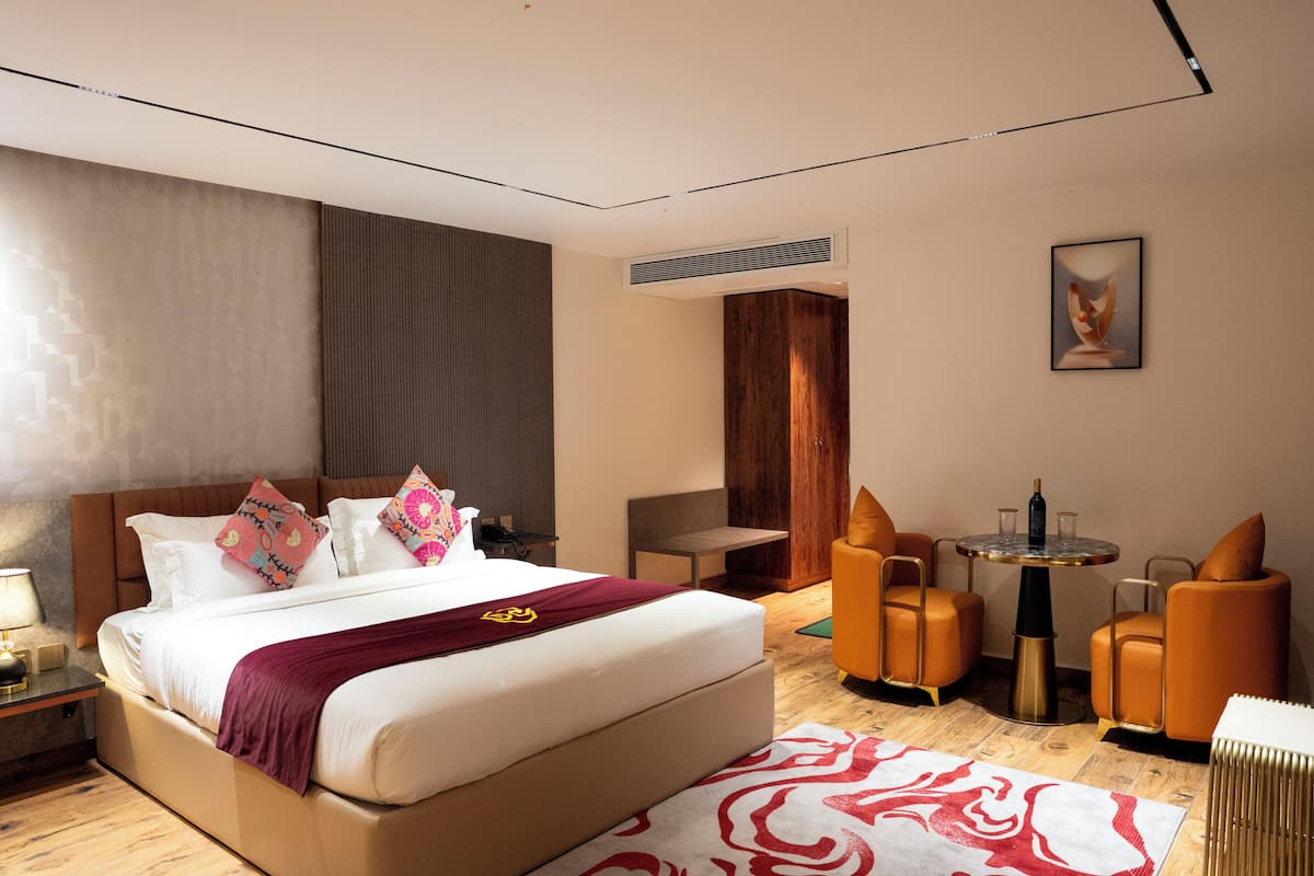 A modern hotel room with a large bed, a small table with chairs, and a wall-mounted air conditioner.