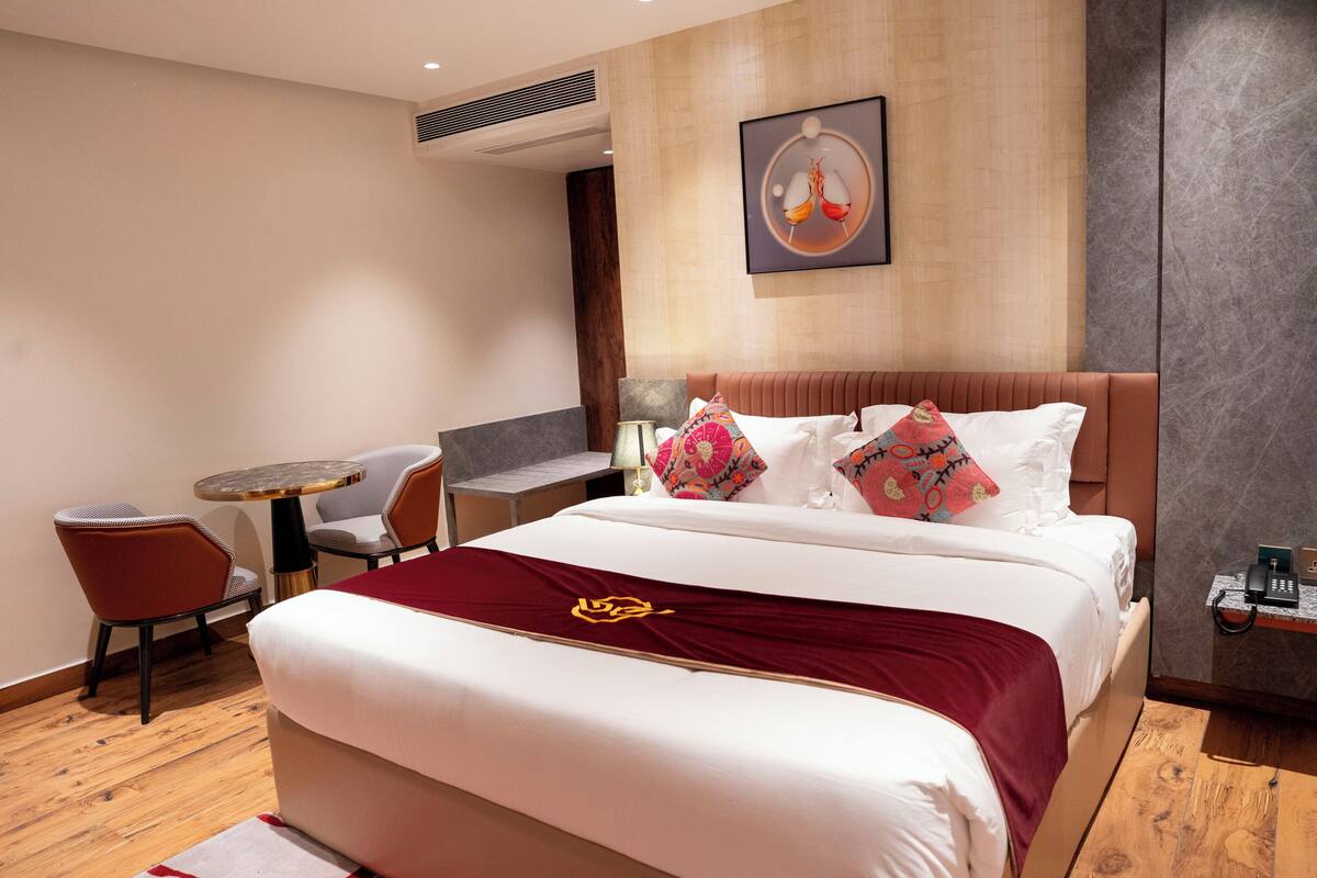 A hotel room with a bed, a small table with chairs, a desk, and a wall-mounted phone.