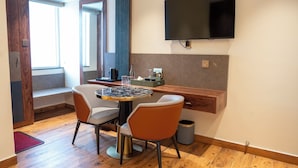 A modern room with a wooden floor, a round table with chairs, a flat-screen TV mounted on the wall, and a window with a view. - Hotel Golden Amulya Rest Wings (Bengaluru)