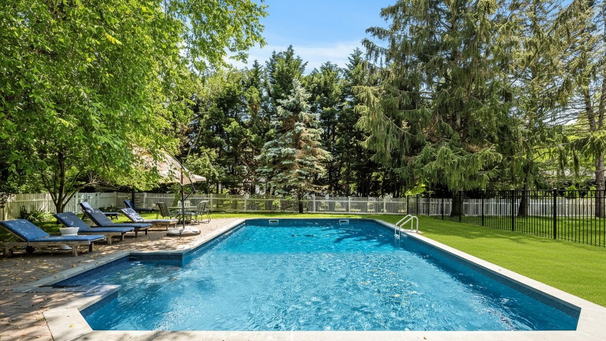 A rectangular swimming pool with a paved deck, surrounded by a black metal fence.