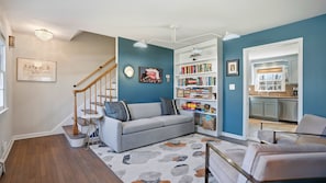 Ein Wohnzimmer mit grauem Sofa, Couchtisch, Bücherregal und einer Treppe.