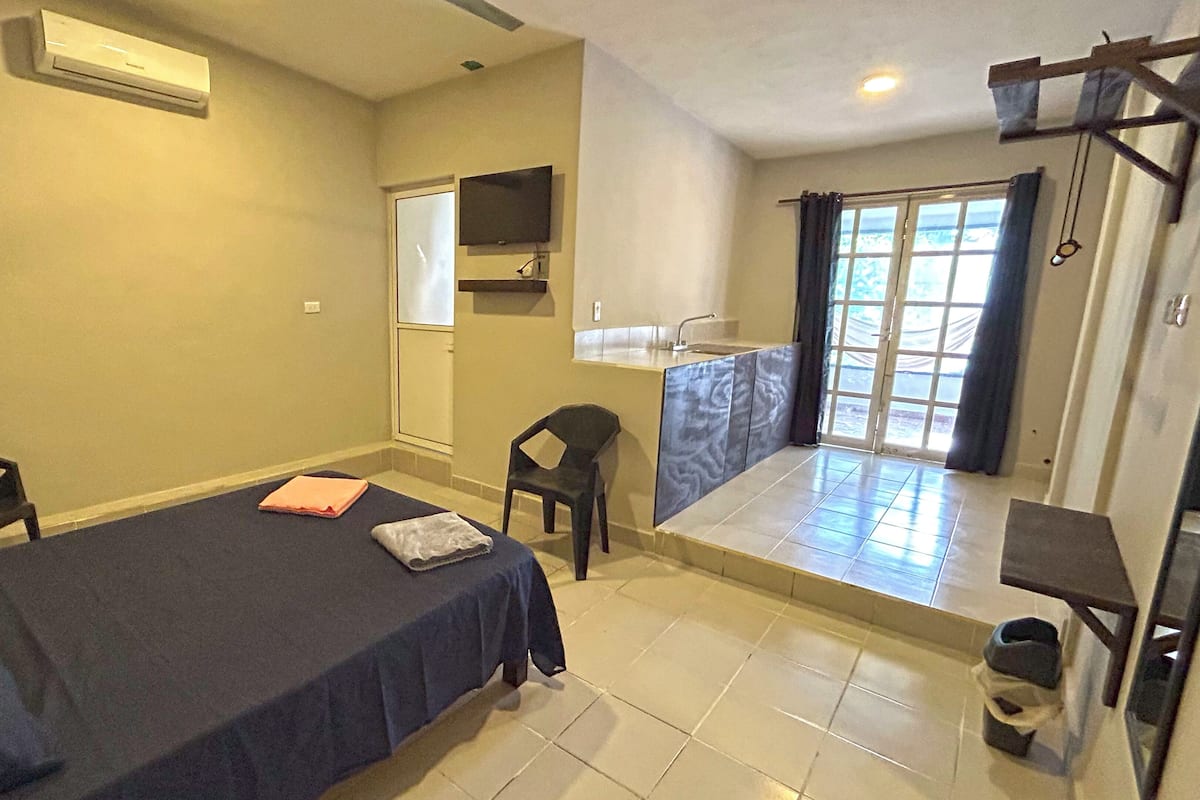 Una habitación con una cama, un escritorio, una silla, una mesita, una ventana y una puerta.