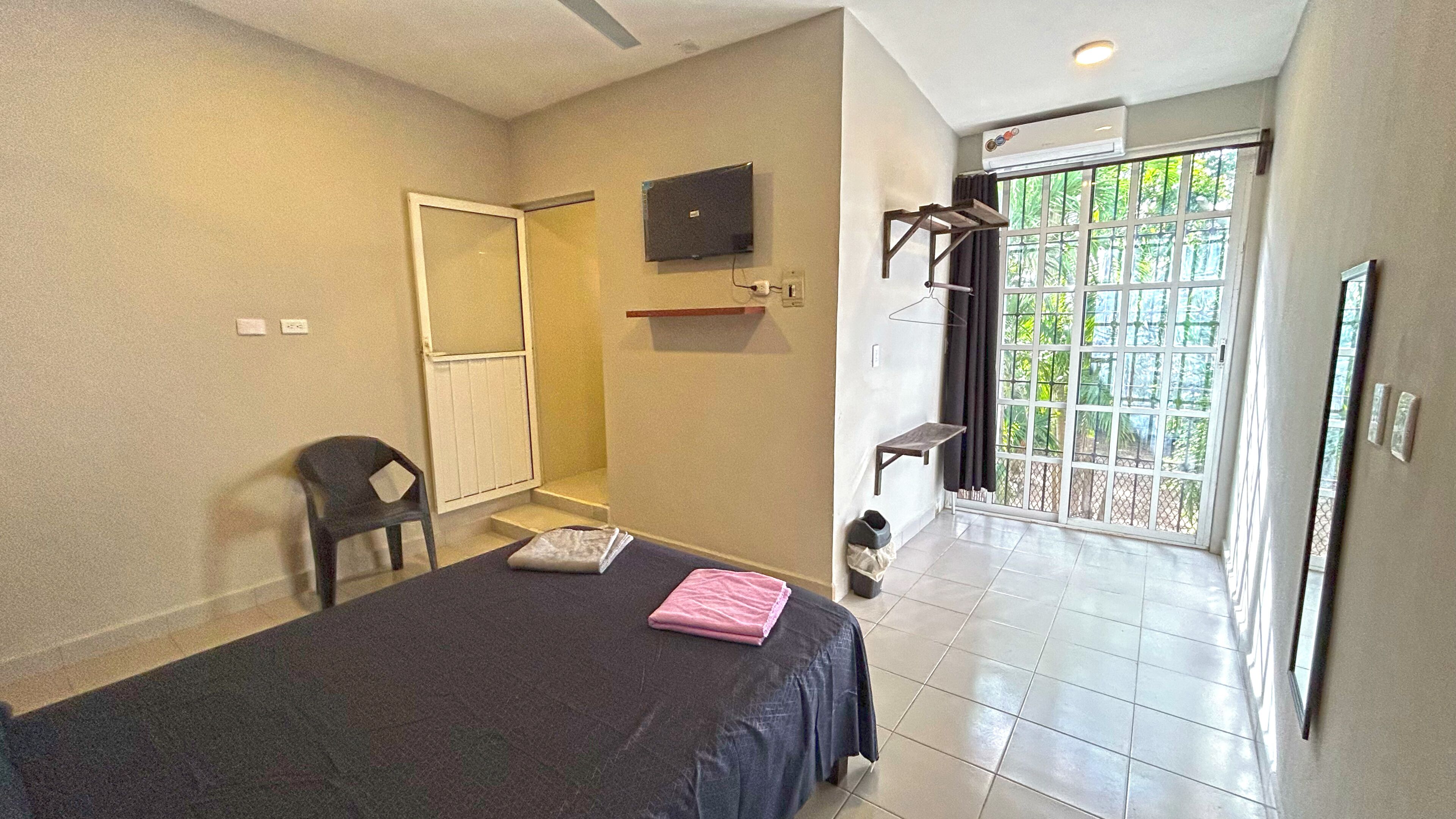 A bedroom with a bed, a chair, a TV, a window, and an air conditioning unit.