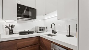 Eine moderne Küche mit weißen Schränken, integriertem Mikrowellenherd, Toaster, Spüle mit schwarzem Wasserhahn und Geschirrspüler.