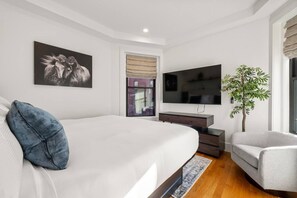 Un dormitorio moderno con una cama grande, televisión, planta y ventana.