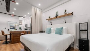 Una habitación de hotel moderna con una cama grande, un escritorio con silla, una zona de estar pequeña y una kitchenette.