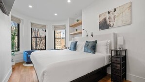 Ein modernes Schlafzimmer mit einem großen Bett, einem blauen Sessel, einem Nachttisch und einem Bild an der Wand.
