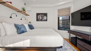 Un dormitorio moderno con una cama grande, un escritorio, un televisor y una ventana con vista a la ciudad.