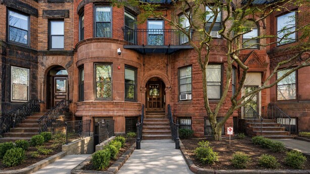 A multi-story brick building with a central entrance, multiple windows, and a tree in the foreground. - Cityscape 1BR Plus: King + Queen Pull-out | Suite 7 (Boston)