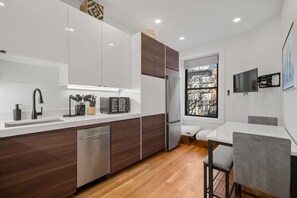 Eine moderne Küche mit weißen Schränken, einem Geschirrspüler, einem Kühlschrank und einem Essbereich mit Tisch und Stühlen.