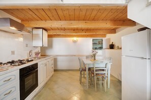 A kitchen with wooden ceiling beams, white cabinets, a dining table with chairs, and a refrigerator.