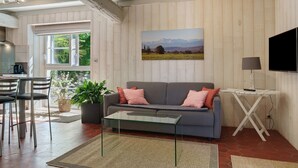 A living room with a sofa, coffee table, TV, and a painting of mountains.