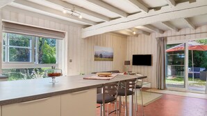 A kitchen with a large island, bar stools, a flat-screen TV, and a window with a view of greenery.