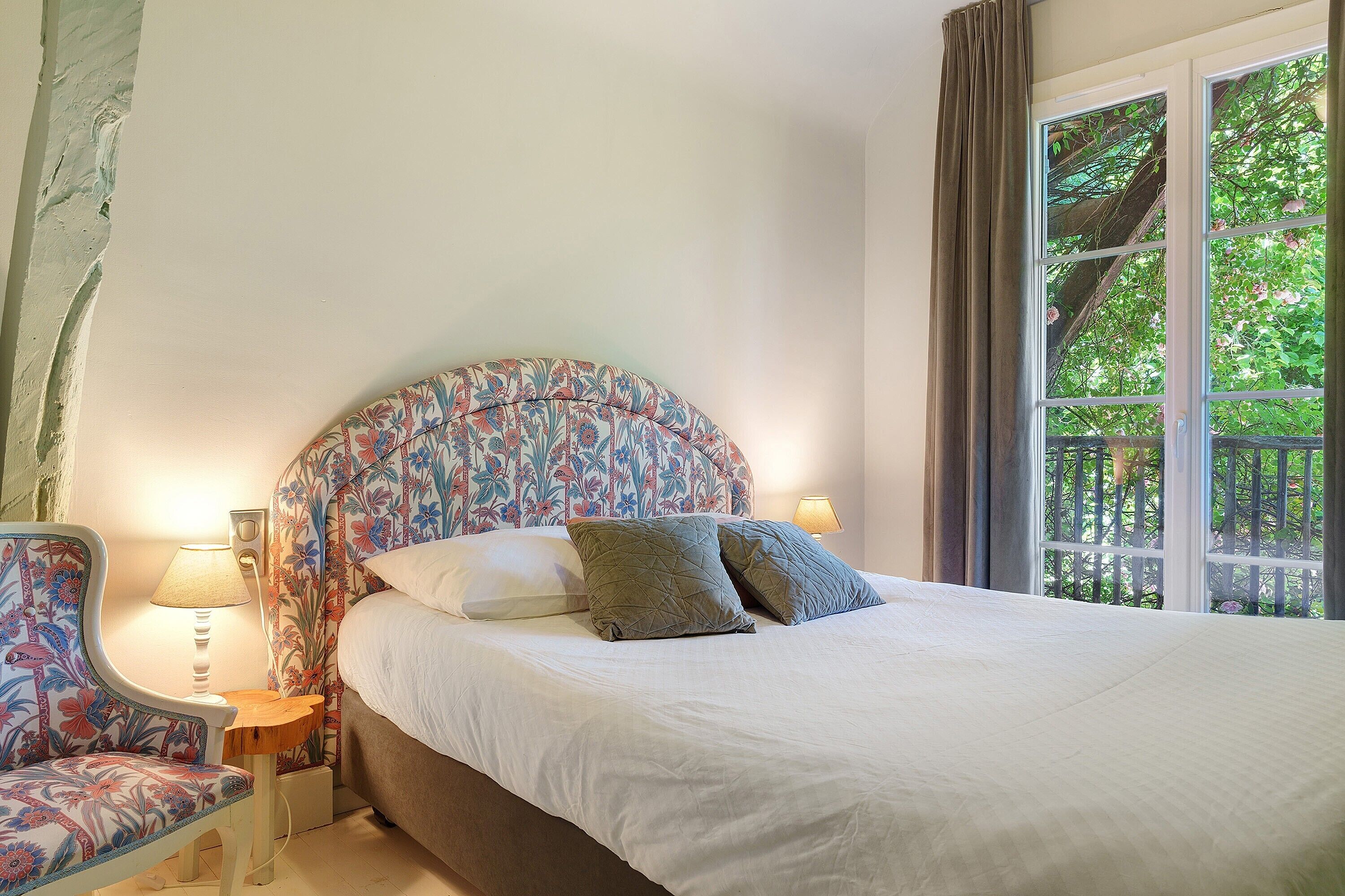 Ein Bett mit einem blumigen Kopfstück, ein Nachttisch mit Lampe und ein Stuhl mit Blumenmuster.