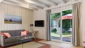 A living room with a sofa, a glass coffee table, a flat-screen TV, and a large sliding glass door leading to an outdoor area with a patio umbrella.