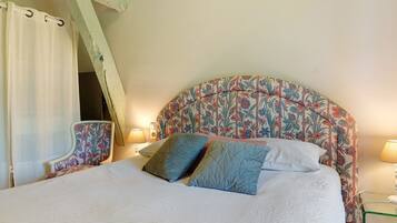 A bed with a floral headboard, a chair with a floral pattern, and a bedside table with a lamp.