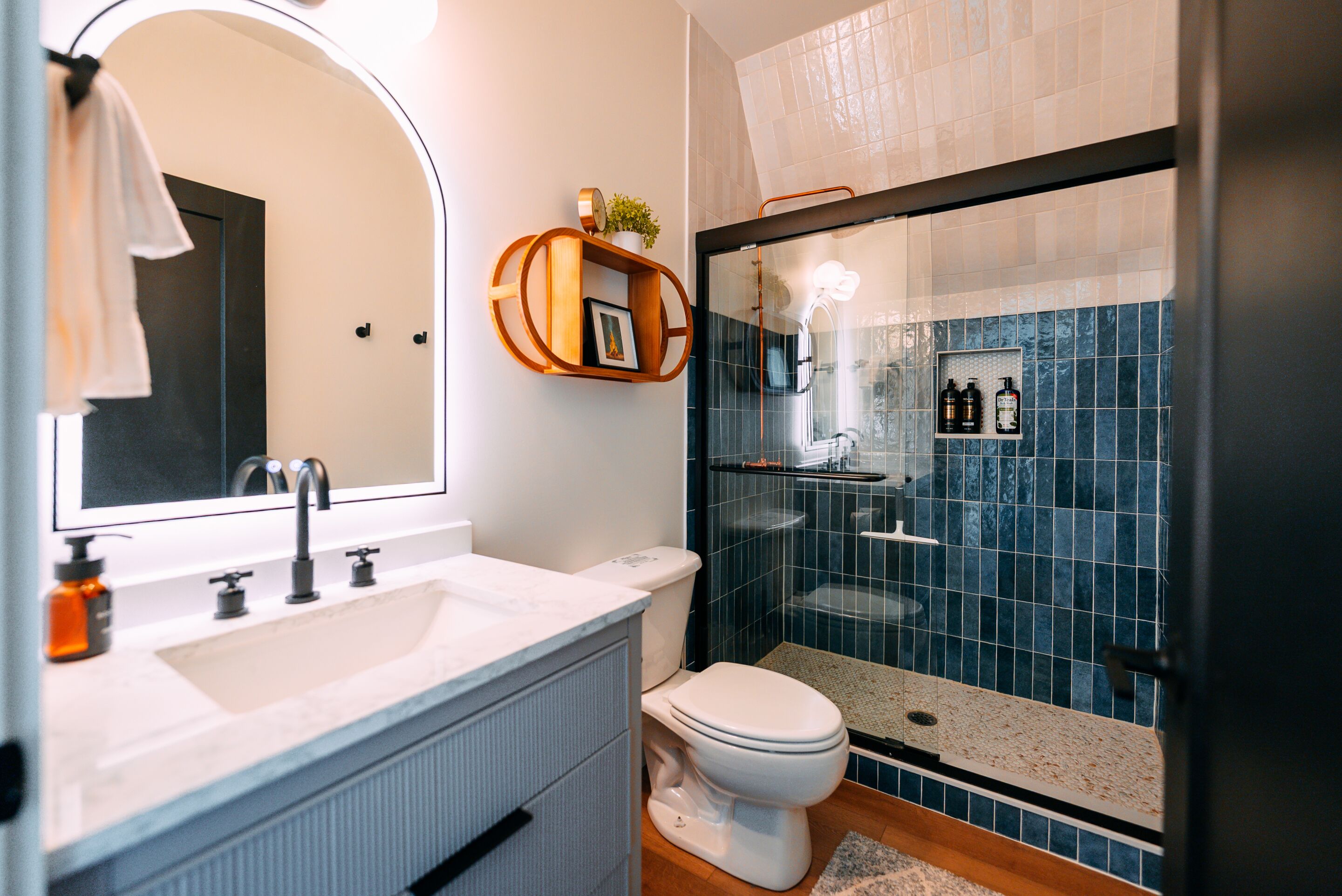 A modern bathroom with a large mirror, a sink, a toilet, and a glass-enclosed shower area.