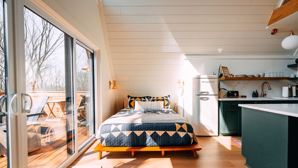 A bedroom with a bed, a view through a sliding door to an outdoor deck, a kitchenette, and a dining area. - Oak Hollow | Hocking Hills, Hot Tub, Romantic (McArthur)